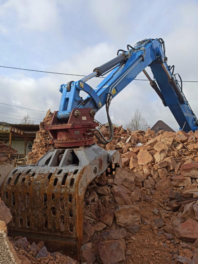 pexels-photo-14446390-14446390 A blue excavator clearing rubble at a construction site under a cloudy sky.